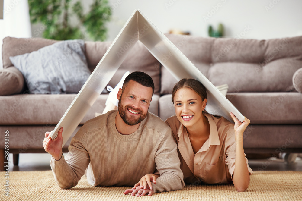 concept housing  young family couple.  man and woman under fake roof in  new home