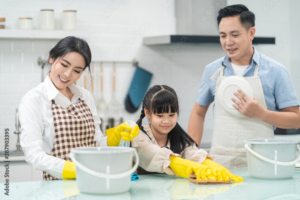 Asian young family teaching their daughter to clean kitchen counter.