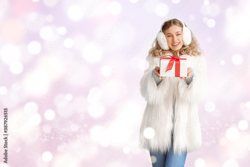 Happy young woman in winter clothes and with Christmas gift on color background