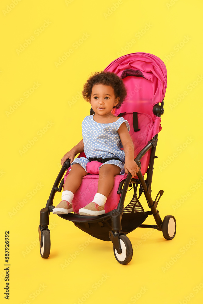 Cute African-American baby in stroller on color background