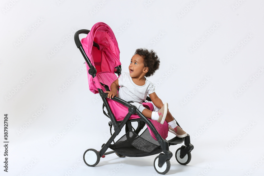 Cute African-American baby in stroller on light background