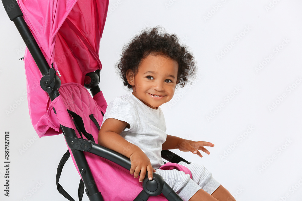 Cute African-American baby in stroller on light background