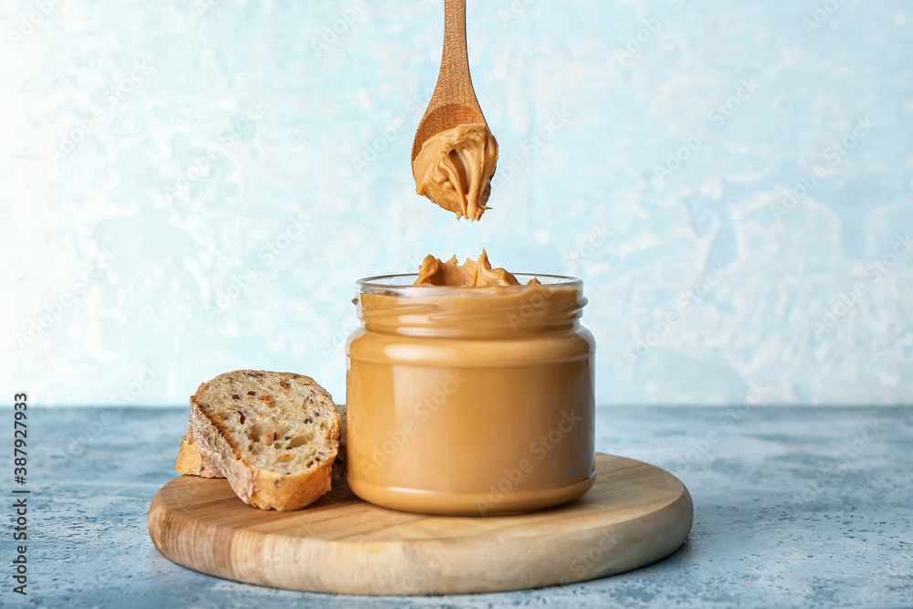 Jar with tasty peanut butter and sliced bread on table