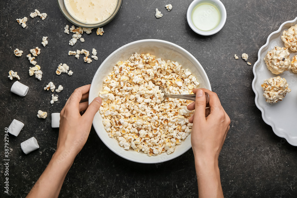 Woman making tasty popcorn balls on dark background