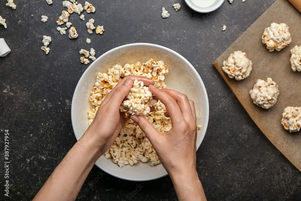 Woman making tasty popcorn balls on dark background