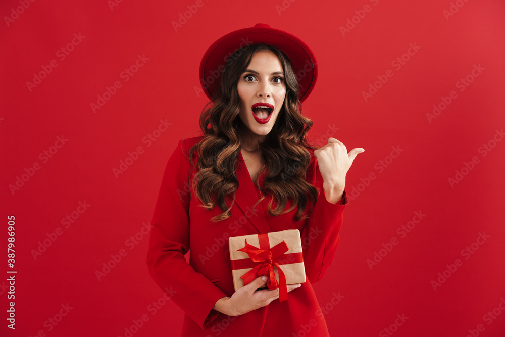 Surprised beautiful woman pointing finger aside and holding gift box