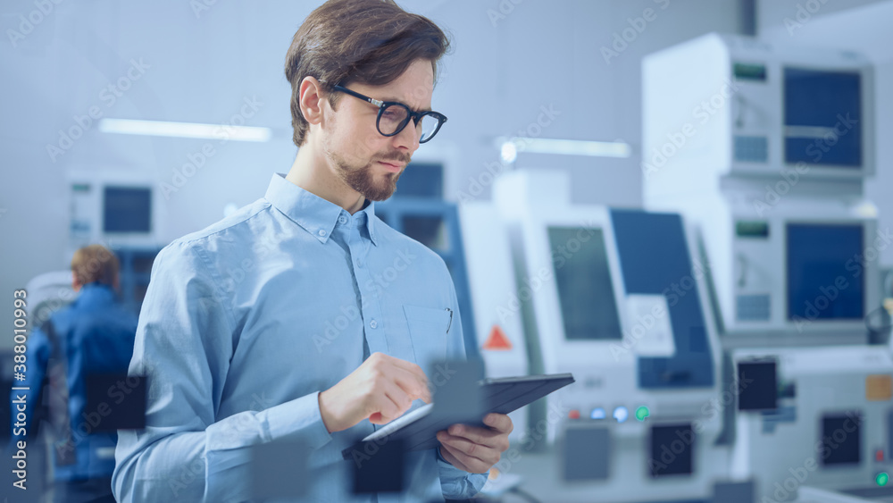 Modern Factory: Industrial Engineer Standing in Facility Workshop, Using Digital Computer, Inspectin