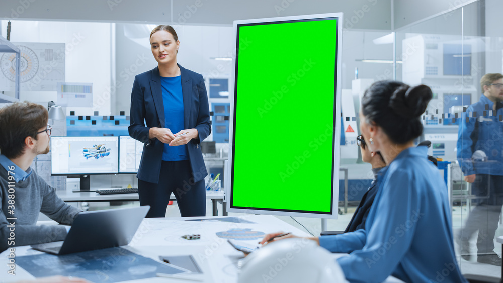 Modern Industrial Factory Meeting: Confident Female Engineer Uses Interactive Green Mock-up Screen W