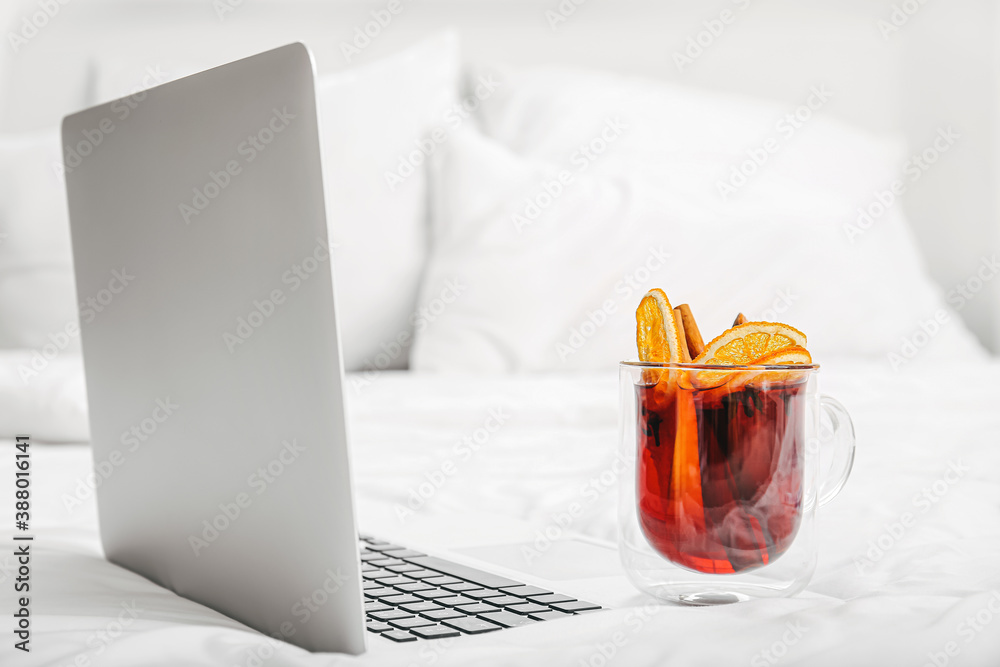 Laptop and mulled wine on bed