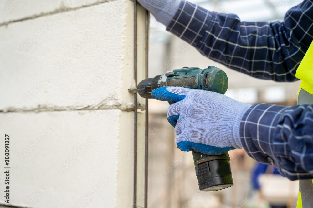 Closeup of a construction worker hands using a drill on a construction site.