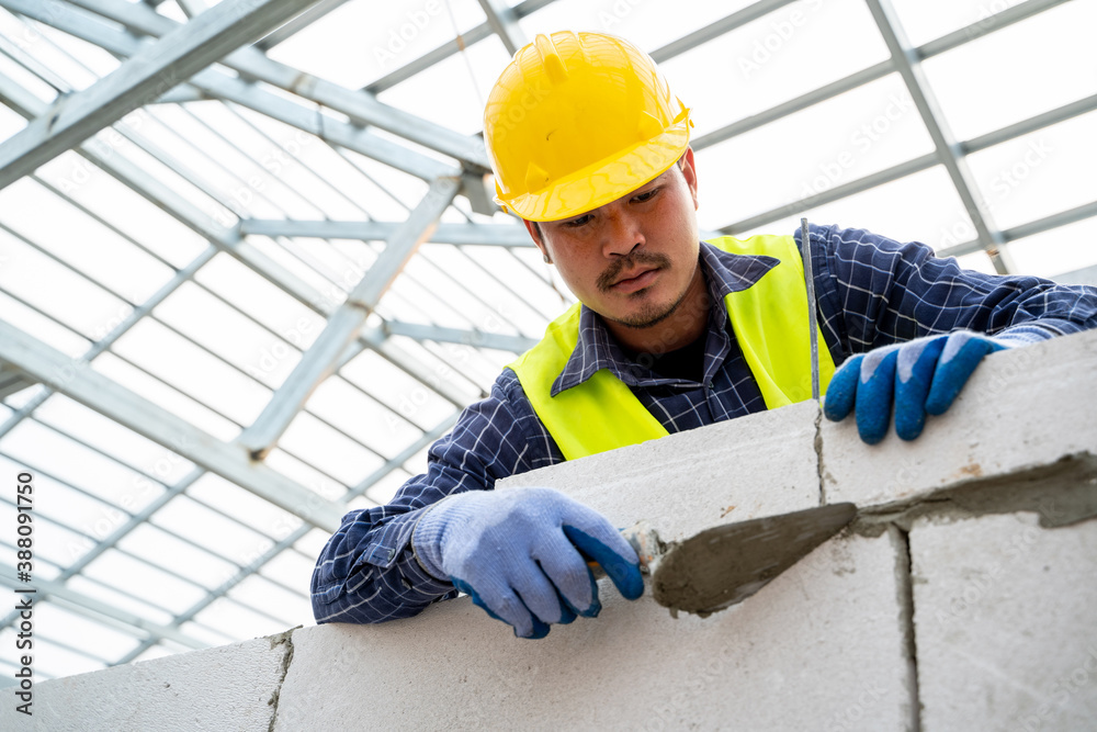 Construction worker puts foam concrete bricks into the wall in the house under construction,Building