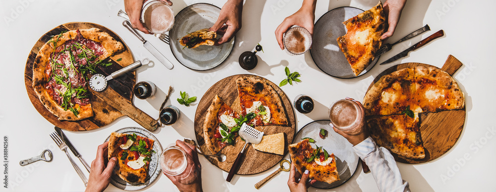 Pizza party for friends. Flat-lay of various pizzas, lager beer and peoples hands with pizza slices 