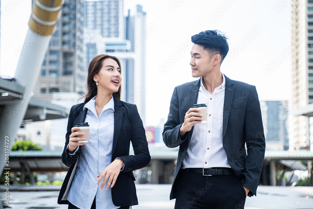 Asian young business couple walking in the city, holding a coffee cup.