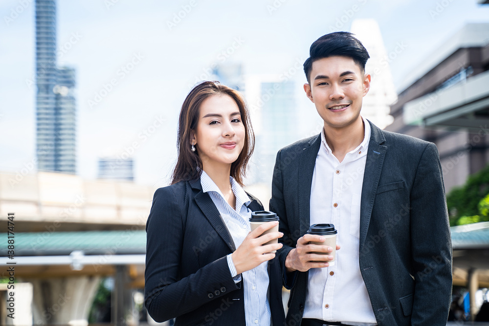 Asian young business couple standing in the city, holding coffee cup.