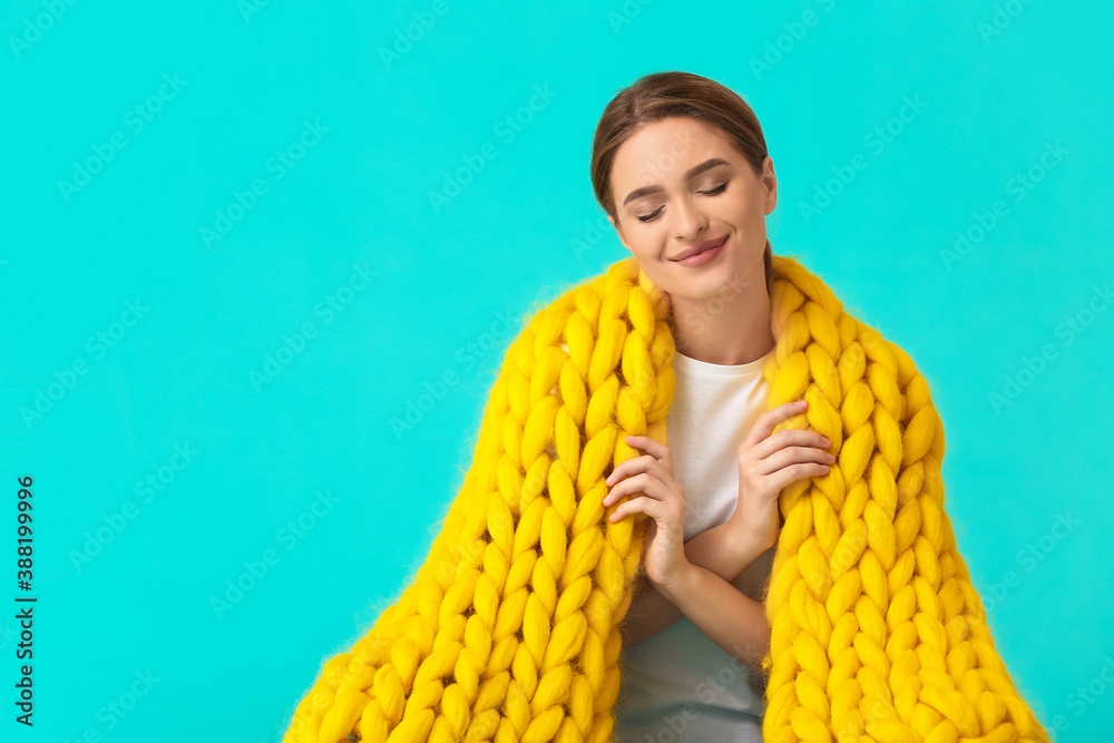 Happy young woman with warm plaid on color background