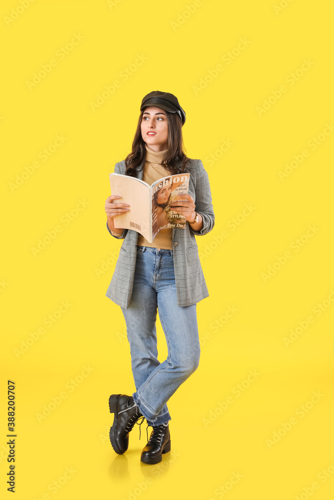 Stylish young woman in autumn clothes and with fashion magazine on color background