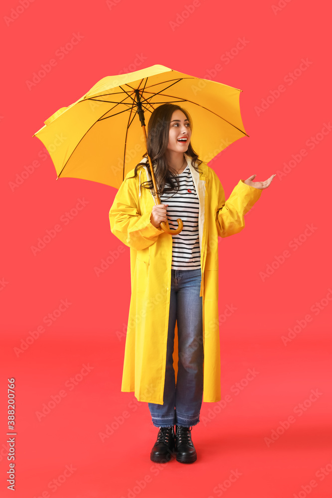 Stylish young woman in raincoat and with umbrella on color background