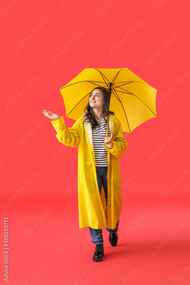 Stylish young woman in raincoat and with umbrella on color background