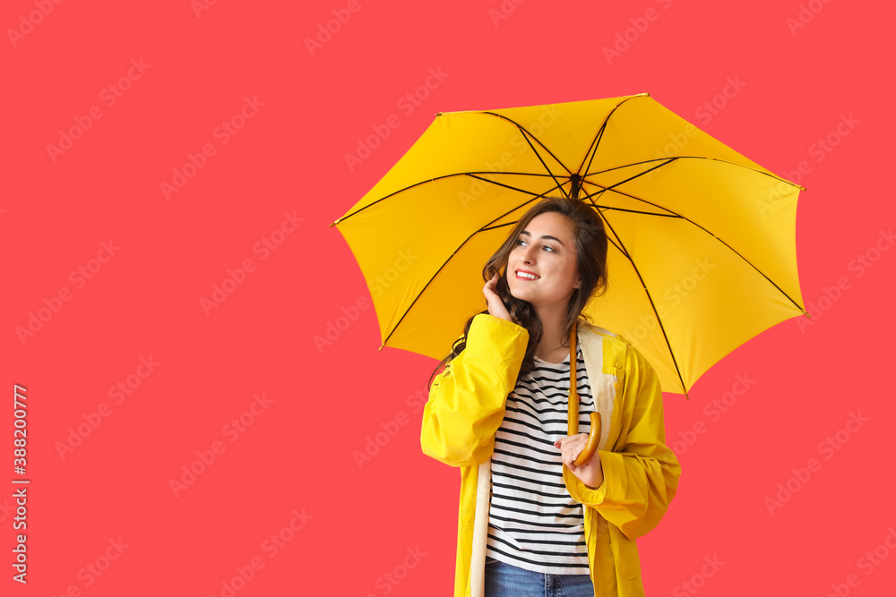 Stylish young woman in raincoat and with umbrella on color background