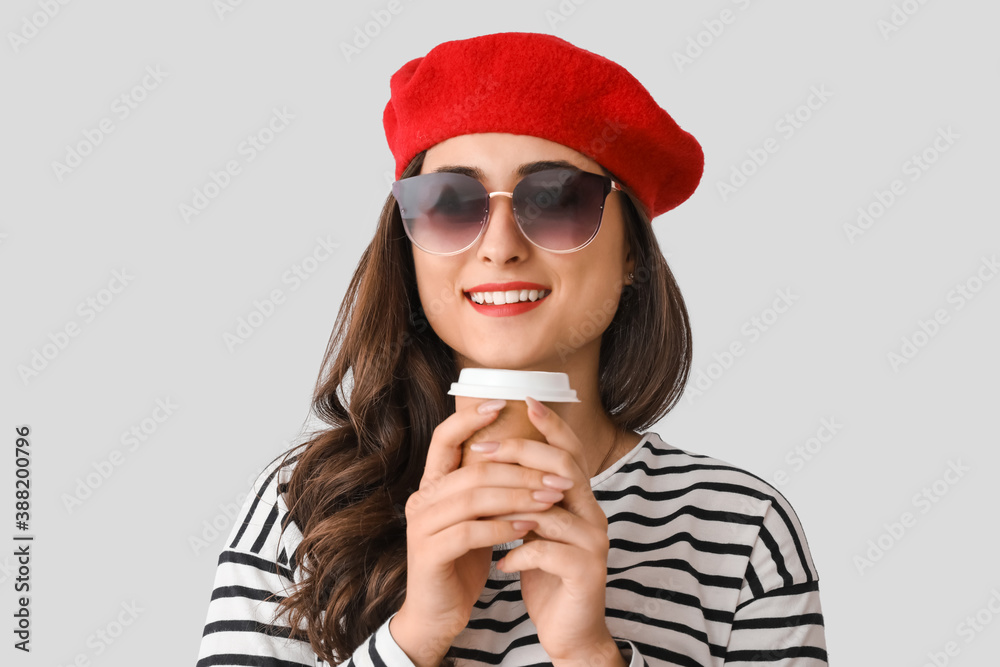 Stylish young woman in autumn clothes and with cup of coffee on light background