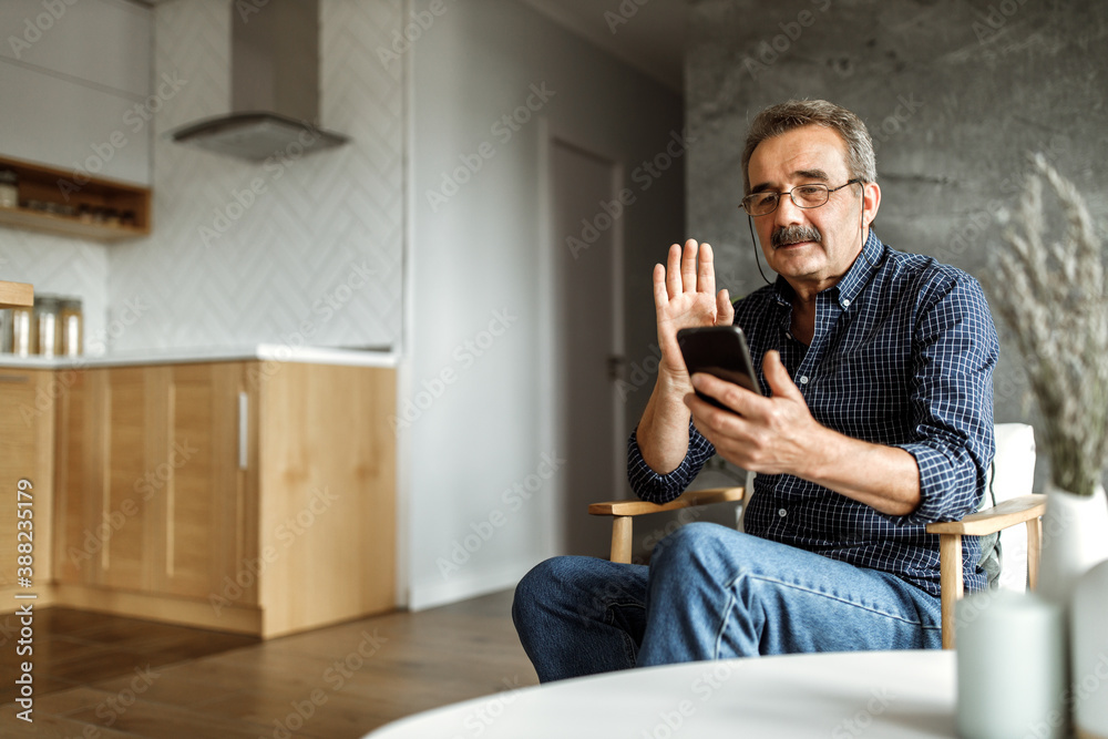 Holding his hand up, looking at phone, saying hello to someone.