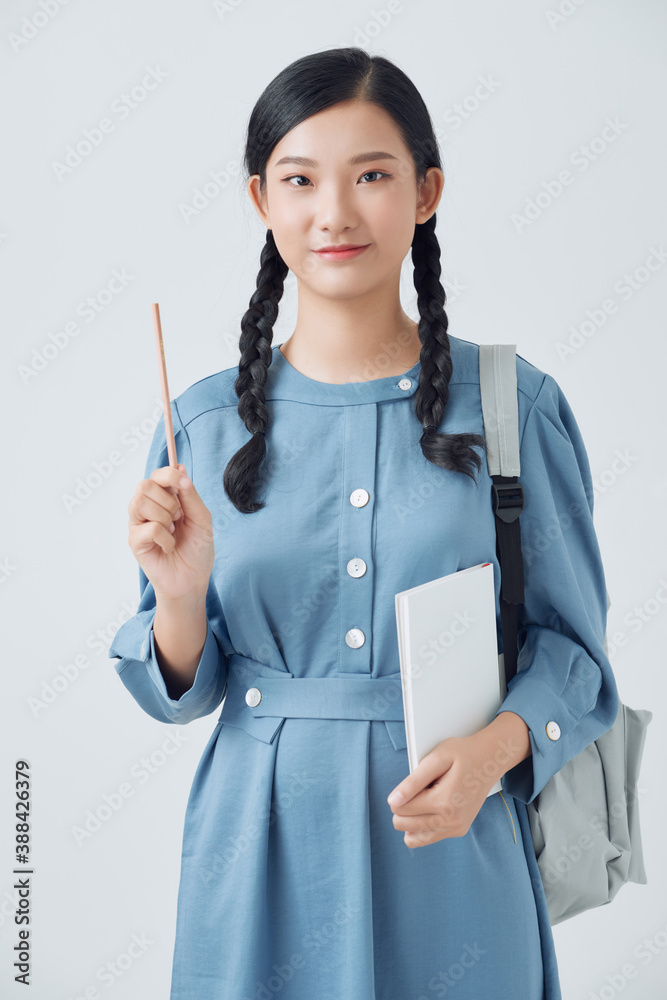 Cheerful young asian teen girl with backpack have an idea and holding notebook isolated on a white b