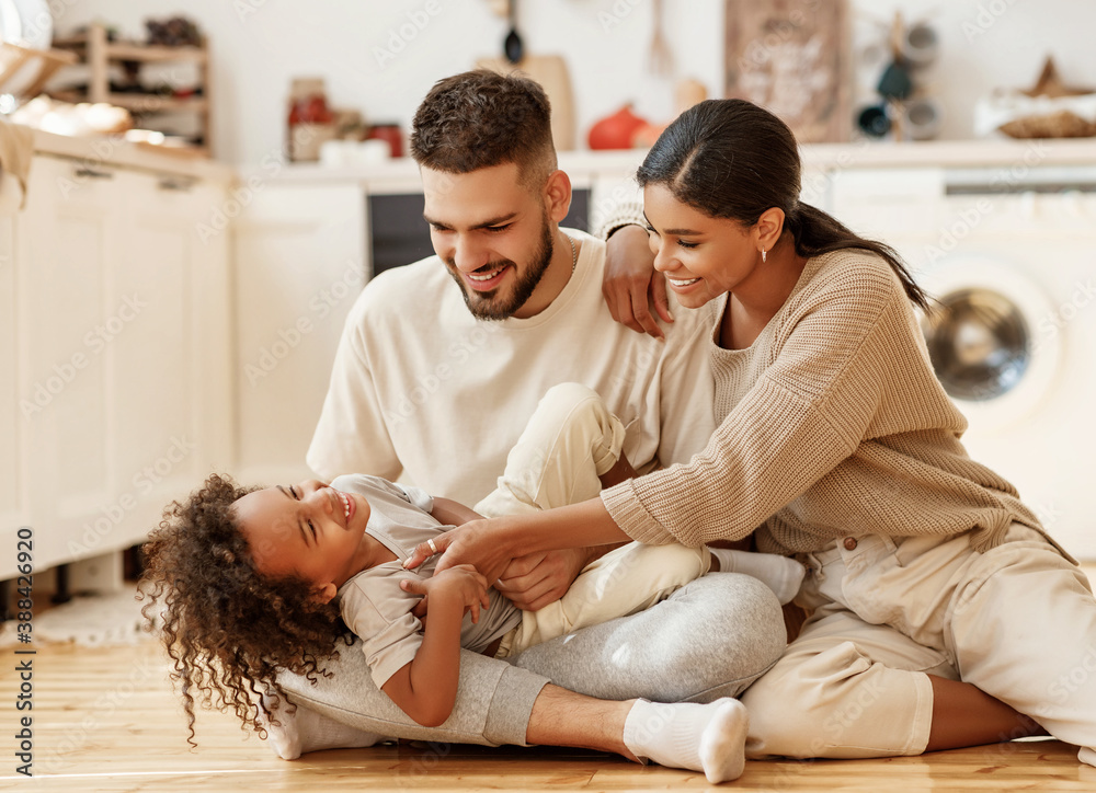 happy multiethnic family mom, dad and child  laughing, playing and tickles    on floor in cozy kitch