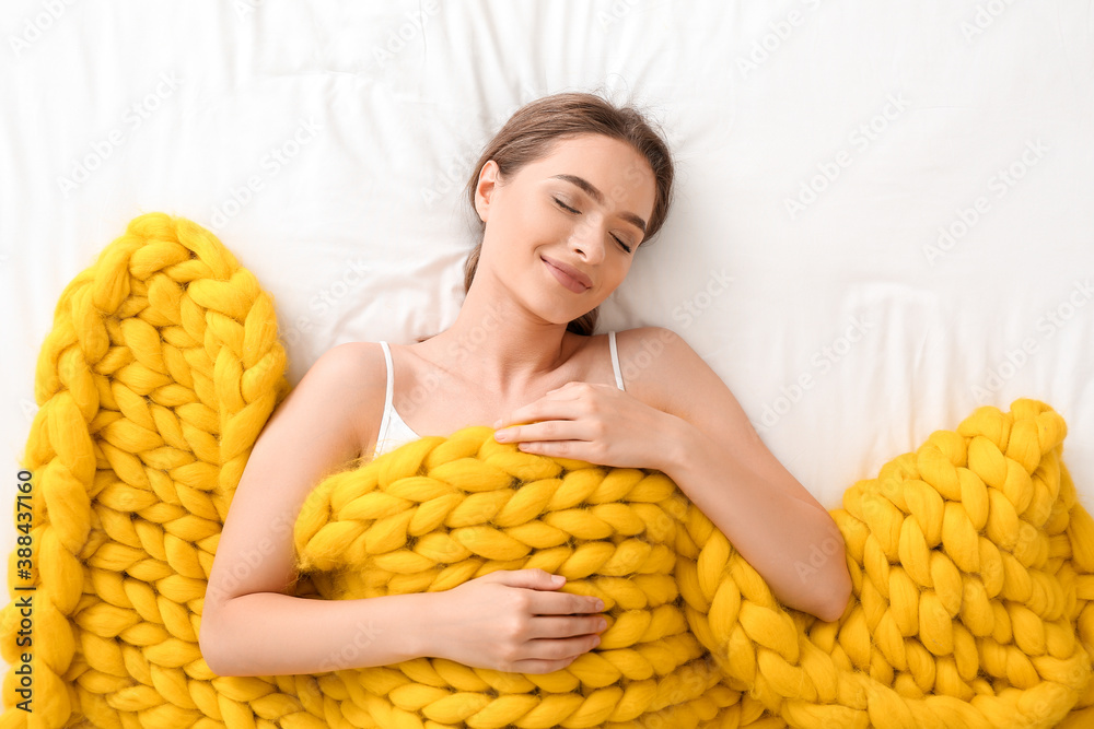 Happy young woman with warm plaid lying on bed, top view