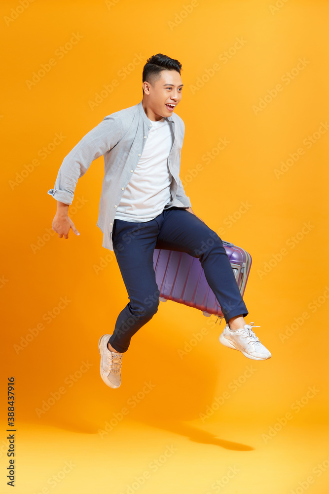 Young creative man is posing with suitcase on yellow background.