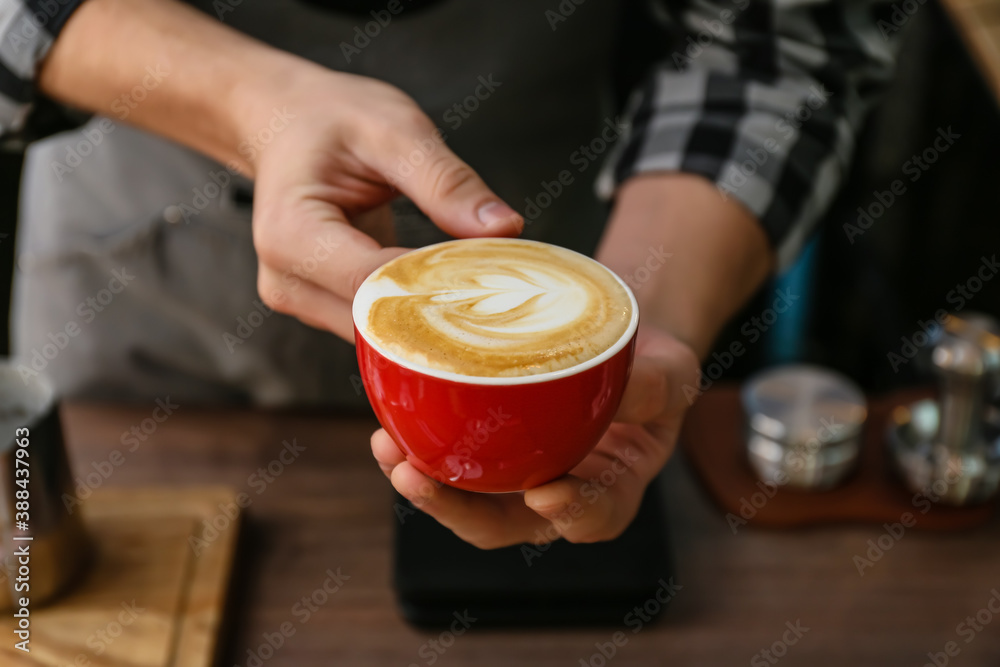 Barista with cup of hot cappuccino in cafe, closeup