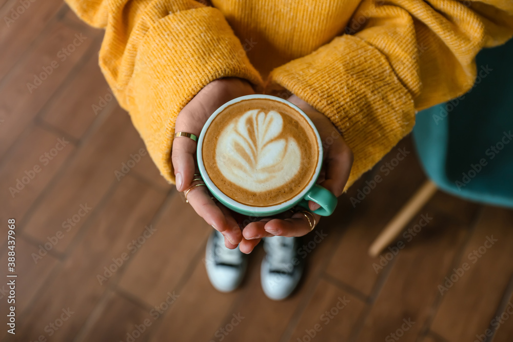 Woman with cup of hot cappuccino in cafe, top view