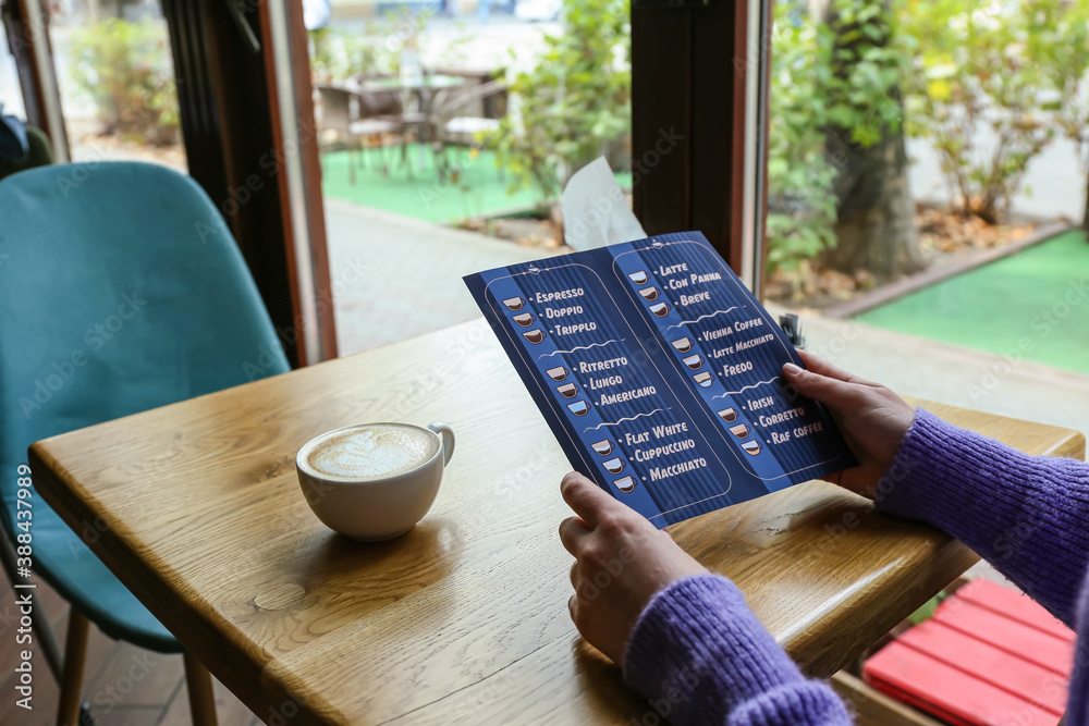 Woman with menu and cup of hot coffee in cafe