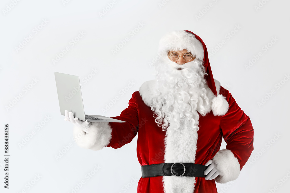 Santa Claus with laptop on light background