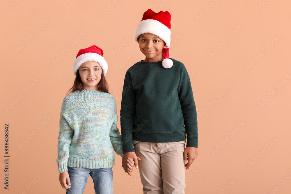 Cute children in winter clothes and Santa hats on color background