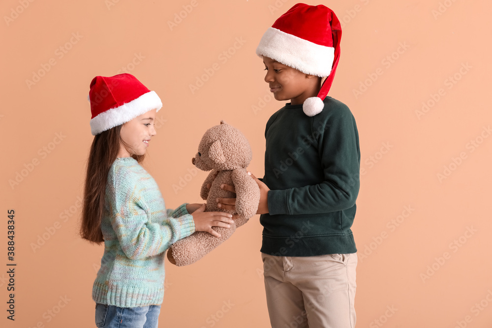 Cute children in winter clothes, Santa hats and with toy on color background