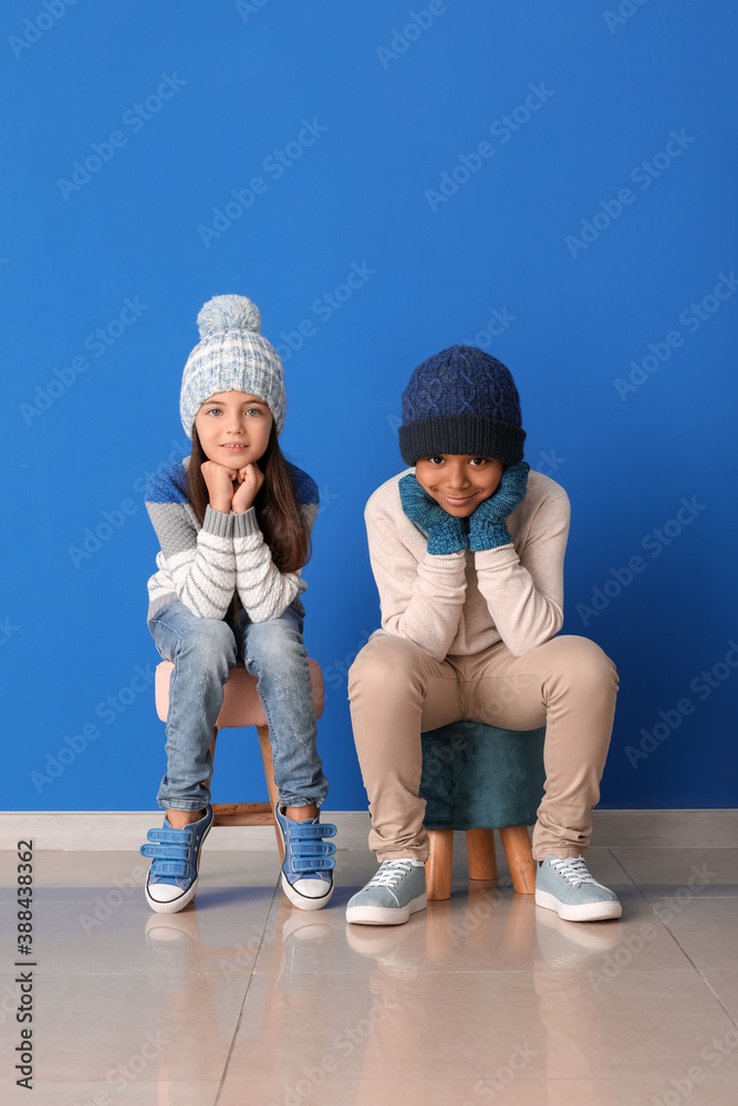 Cute children in winter clothes near color wall