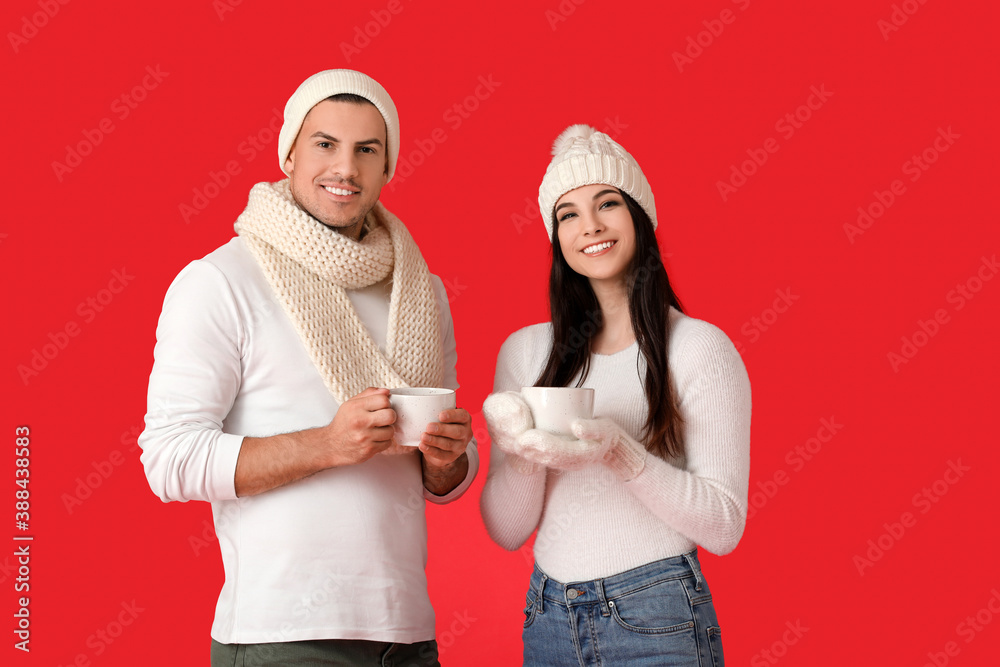 Young couple in winter clothes and with hot tea on color background