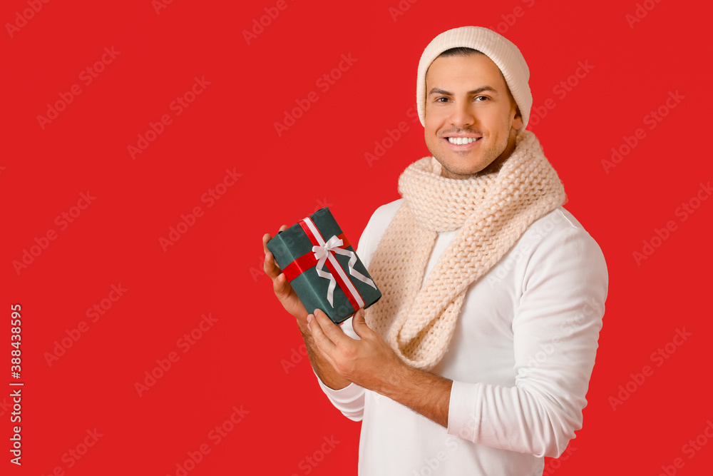 Handsome young man with Christmas gift on color background