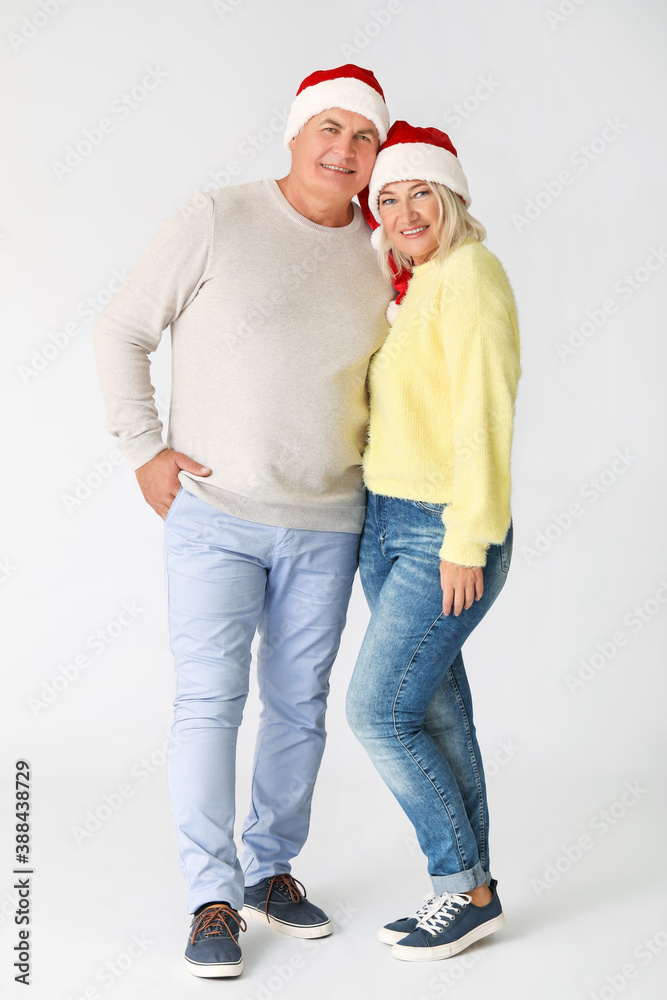 Mature couple in Santa hats on light background