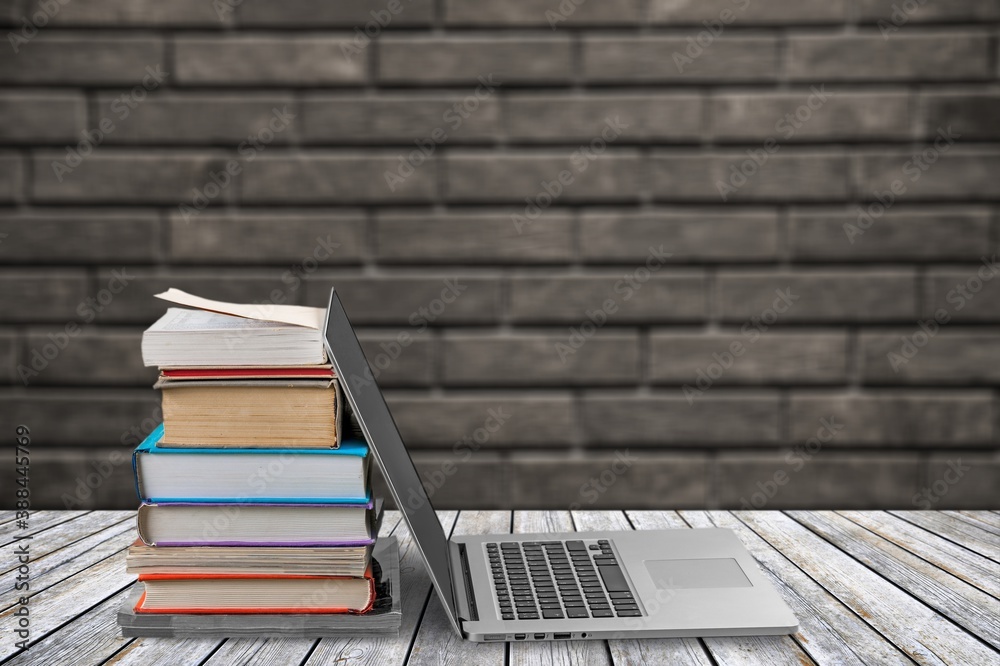 Stack of books with open laptop on table