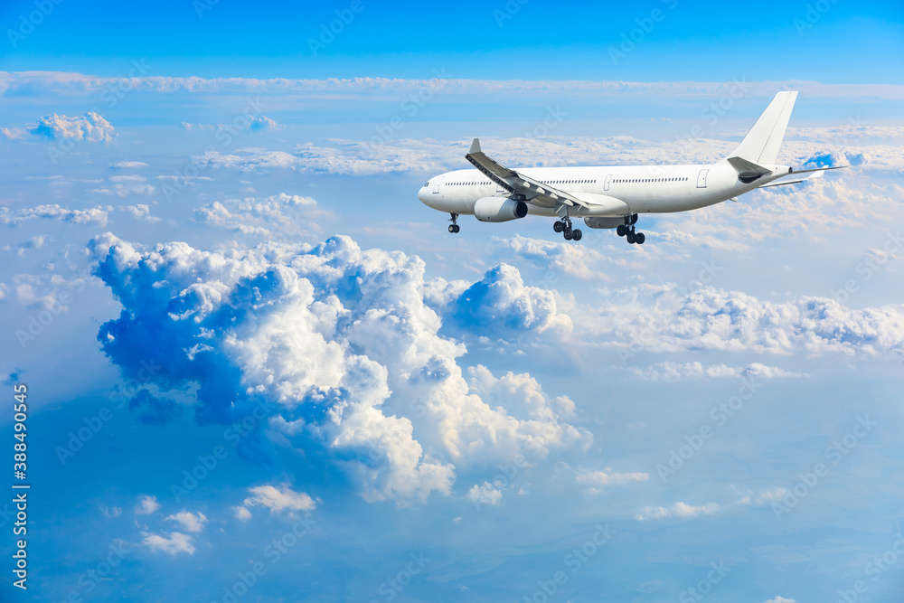 Commercial airplane flying above blue sky and white clouds.