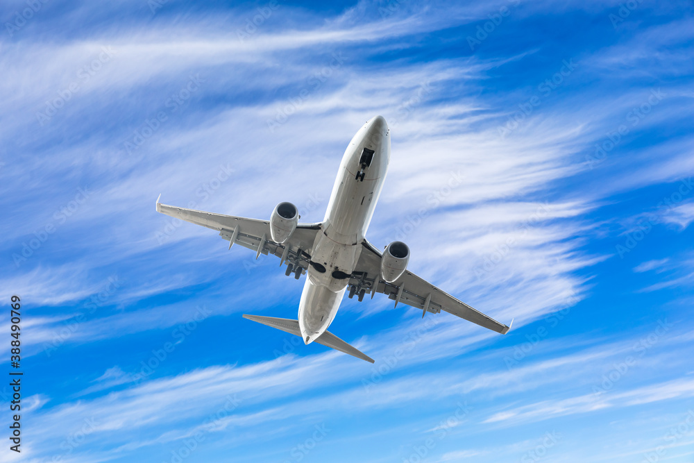 Commercial airplane flying above blue sky and white clouds.