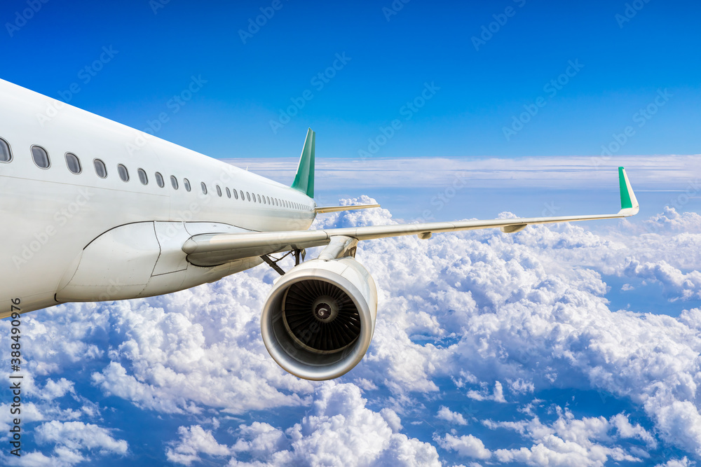 Commercial airplane flying above blue sky and white clouds.