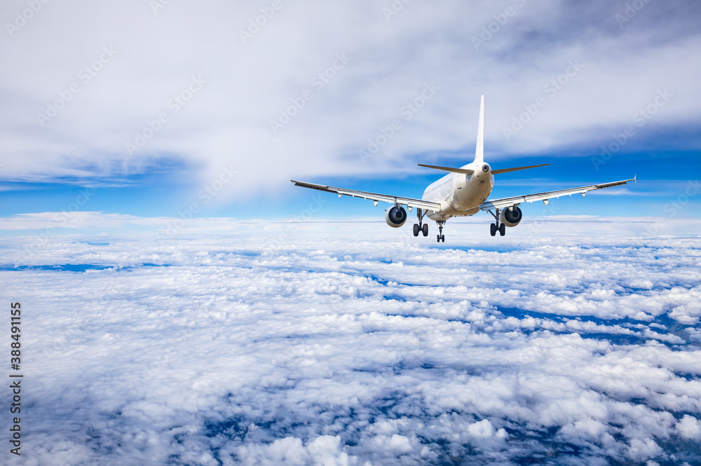 Commercial airplane flying above blue sky and white clouds.