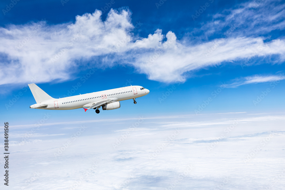 Commercial airplane flying above blue sky and white clouds.