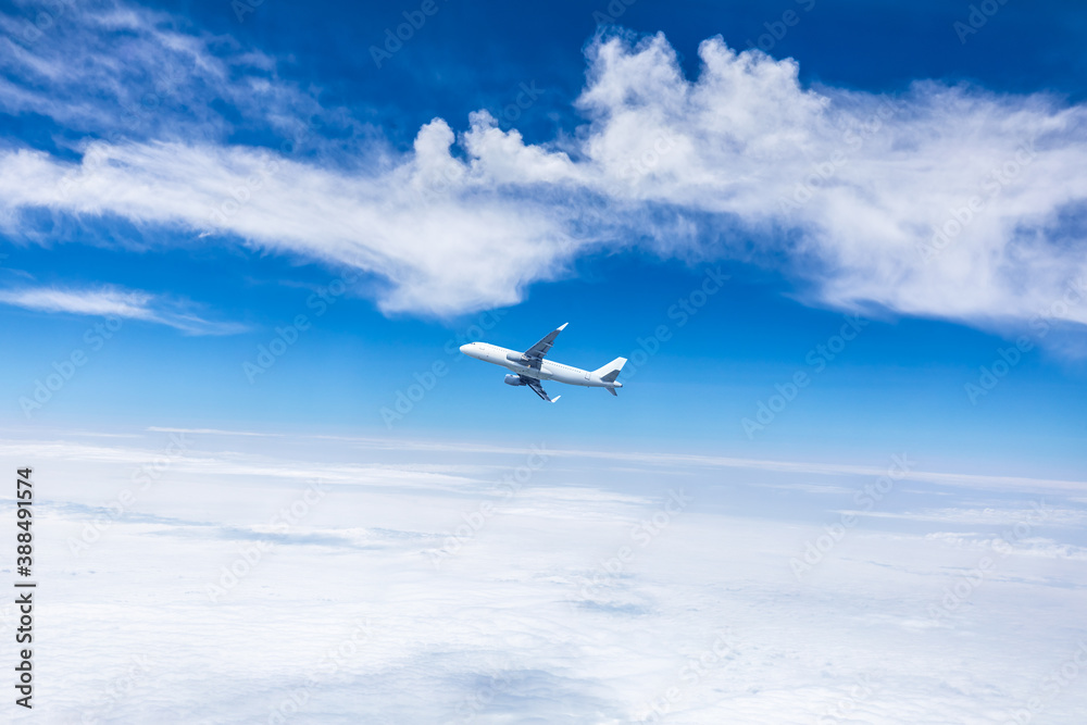 Commercial airplane flying above blue sky and white clouds.