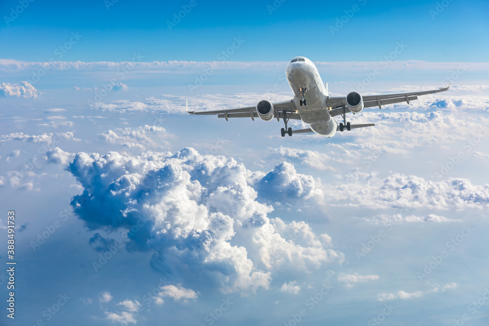 Commercial airplane flying above blue sky and white clouds.