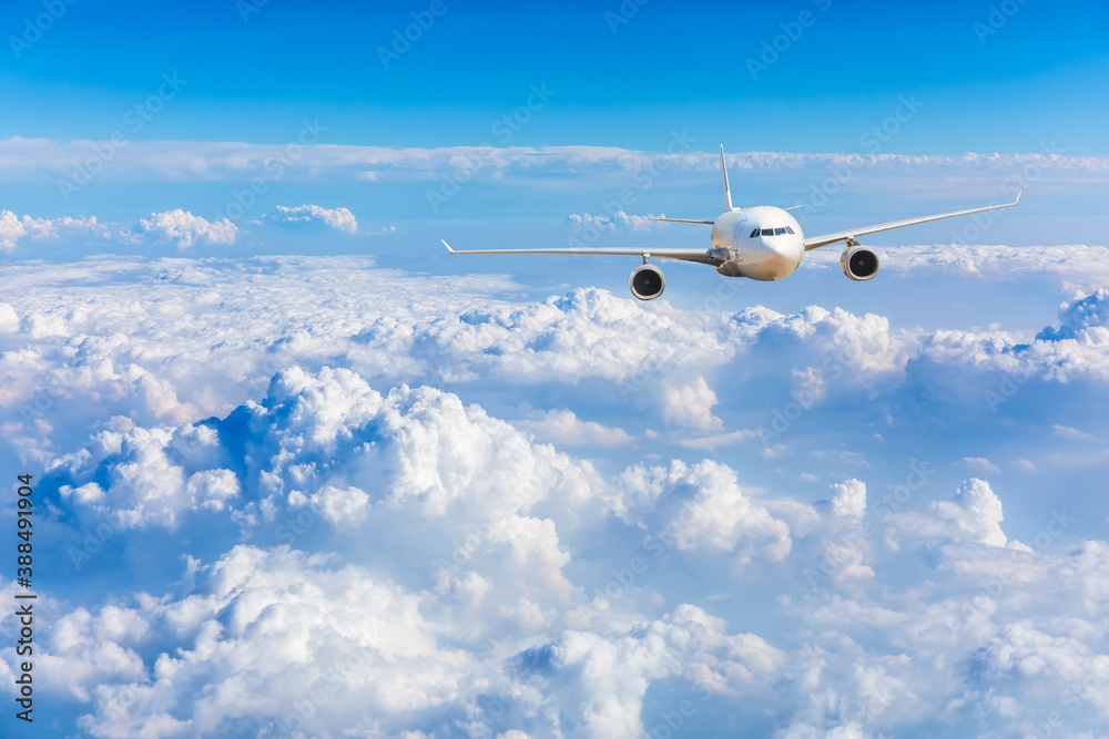 Commercial airplane flying above blue sky and white clouds.