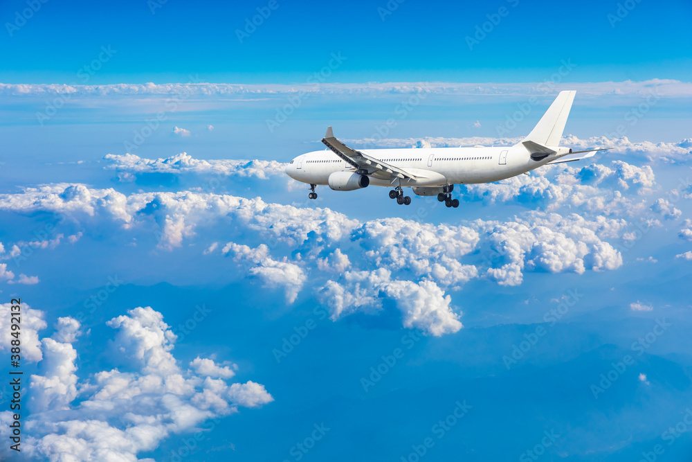 Commercial airplane flying above blue sky and white clouds.