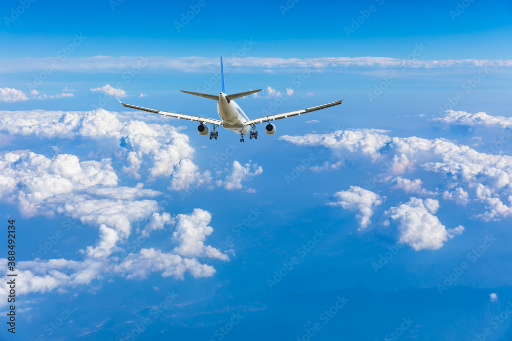 Commercial airplane flying above blue sky and white clouds.